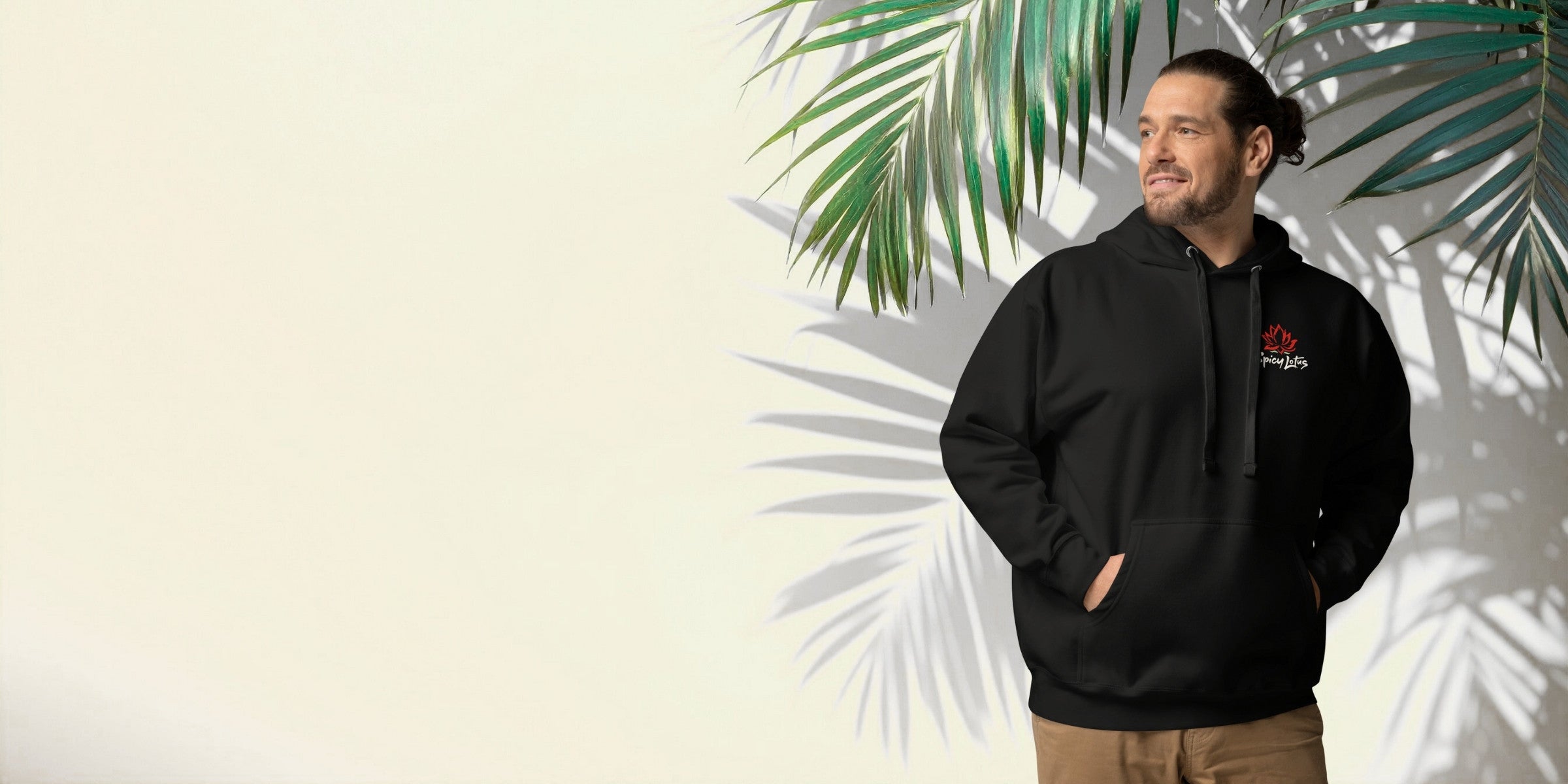 Man wearing a black hoodie in front of a tropical white wall with palm leafs and shadows in the background. 