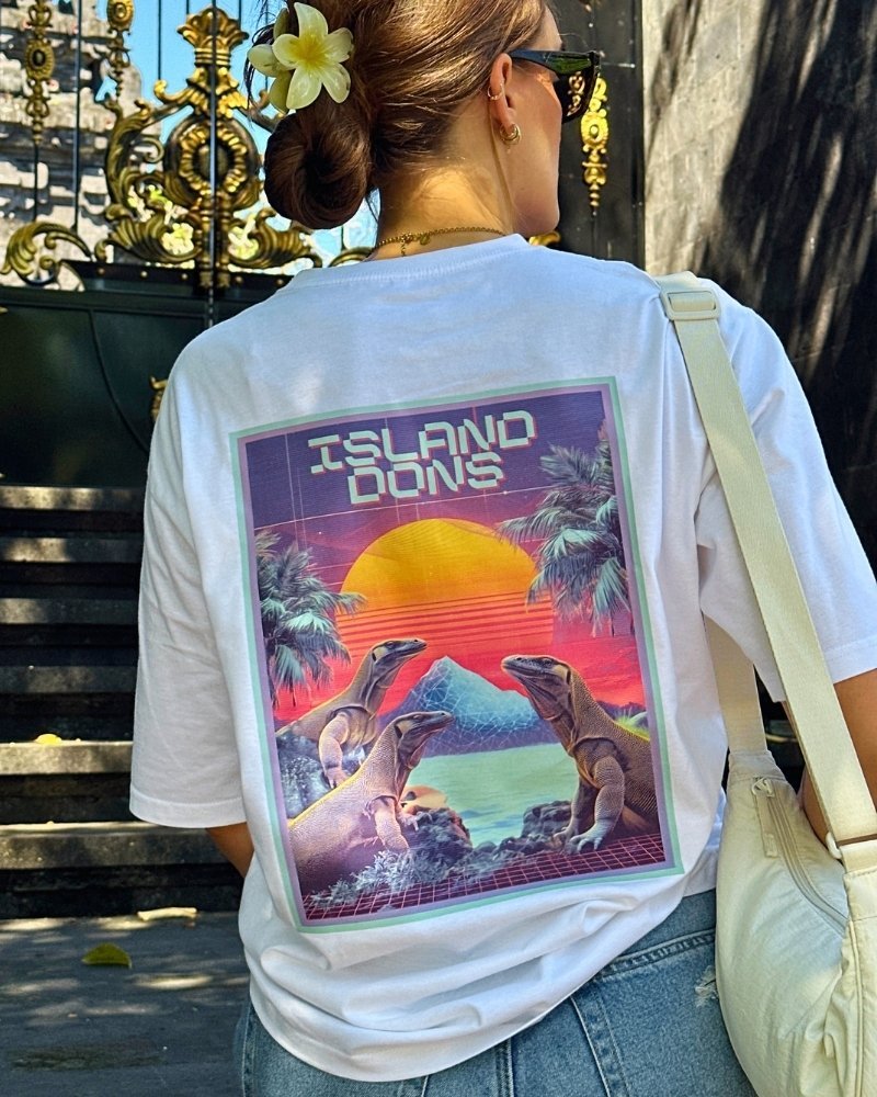 Woman wearing a withe shirt with colorful back design in front of a temple.