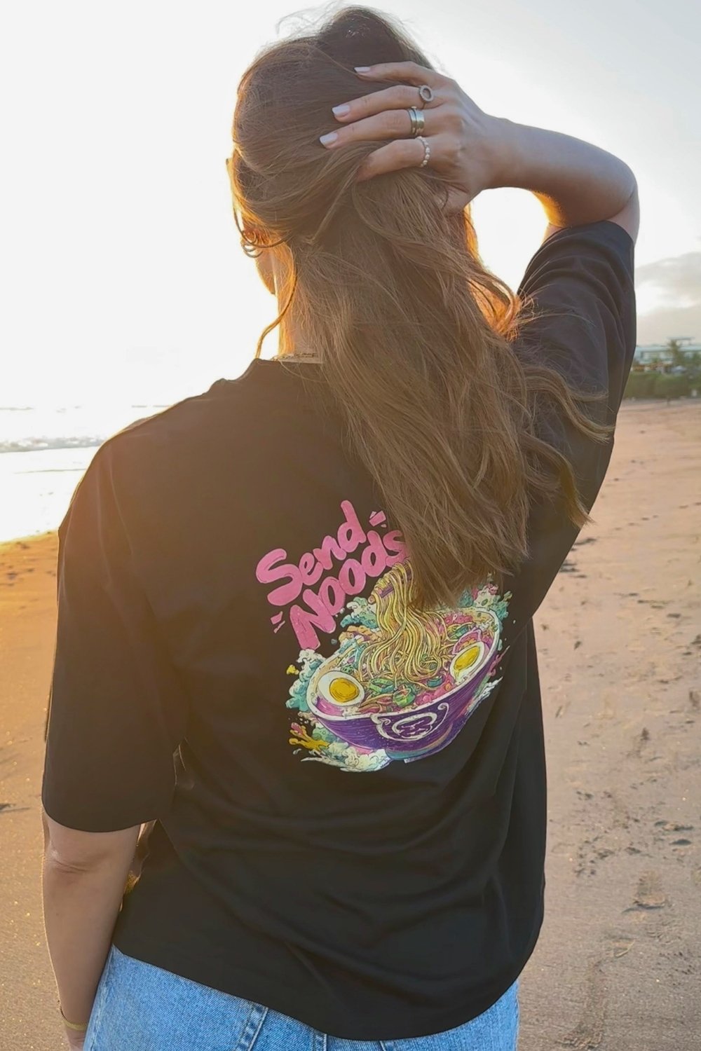 Woman wearing a black Spicy Lotus t-shirt with colorful graphic and text on a beach.