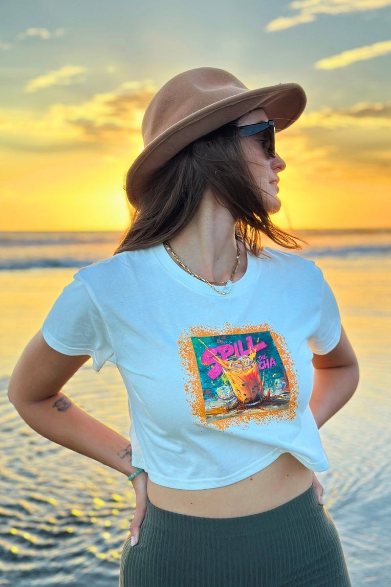 Woman wearing a spicy lotus crop top with a colorful graphic design on a beach at sunset.