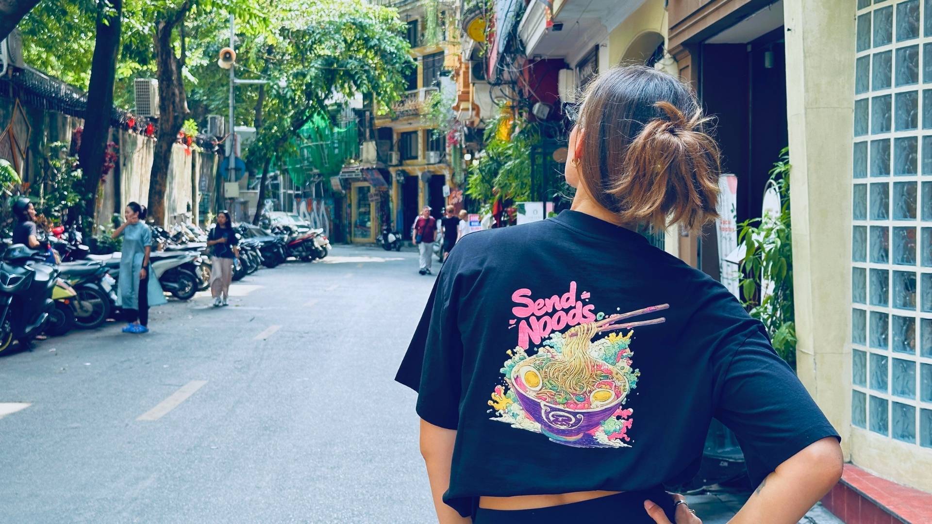 Woman wearing black Spicy Lotus t-shirt with graphic back design standing in a busy Vietnamese street.
