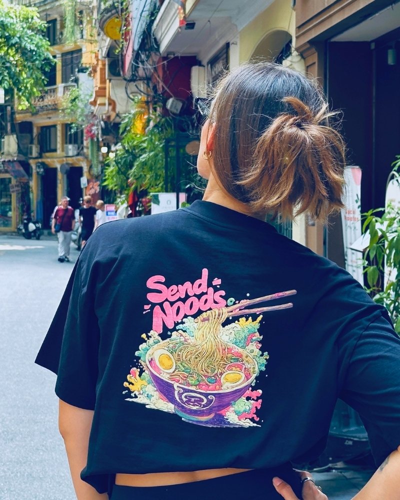 Woman wearing black Spicy Lotus t-shirt with graphic back design standing in a busy Vietnamese street.