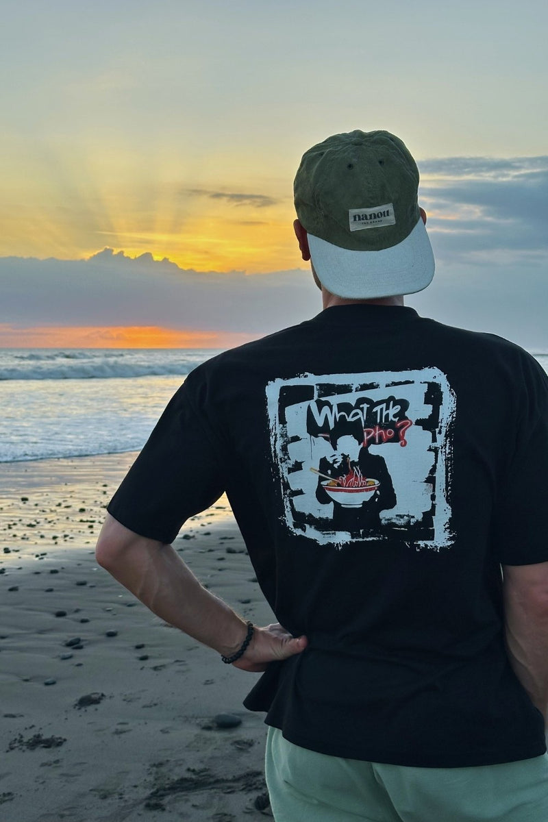 Person wearing a black t-shirt with a graphic Pho design, standing on a beach at sunset.