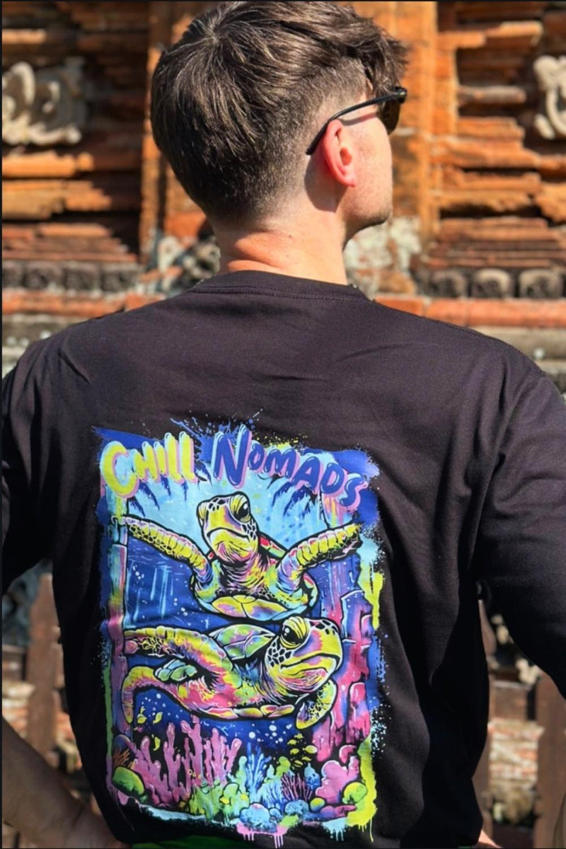 Male model wearing a black spicy lotus shirt with a colorful turtle graphic design on the back, standing against a textured wall.