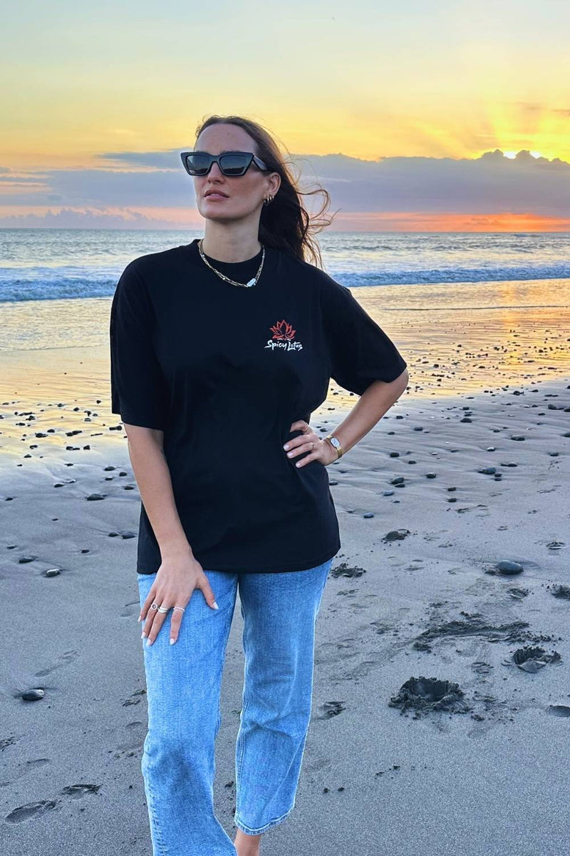 Woman wearing a black t-shirt with a spicy lotus logo on a beach at sunset