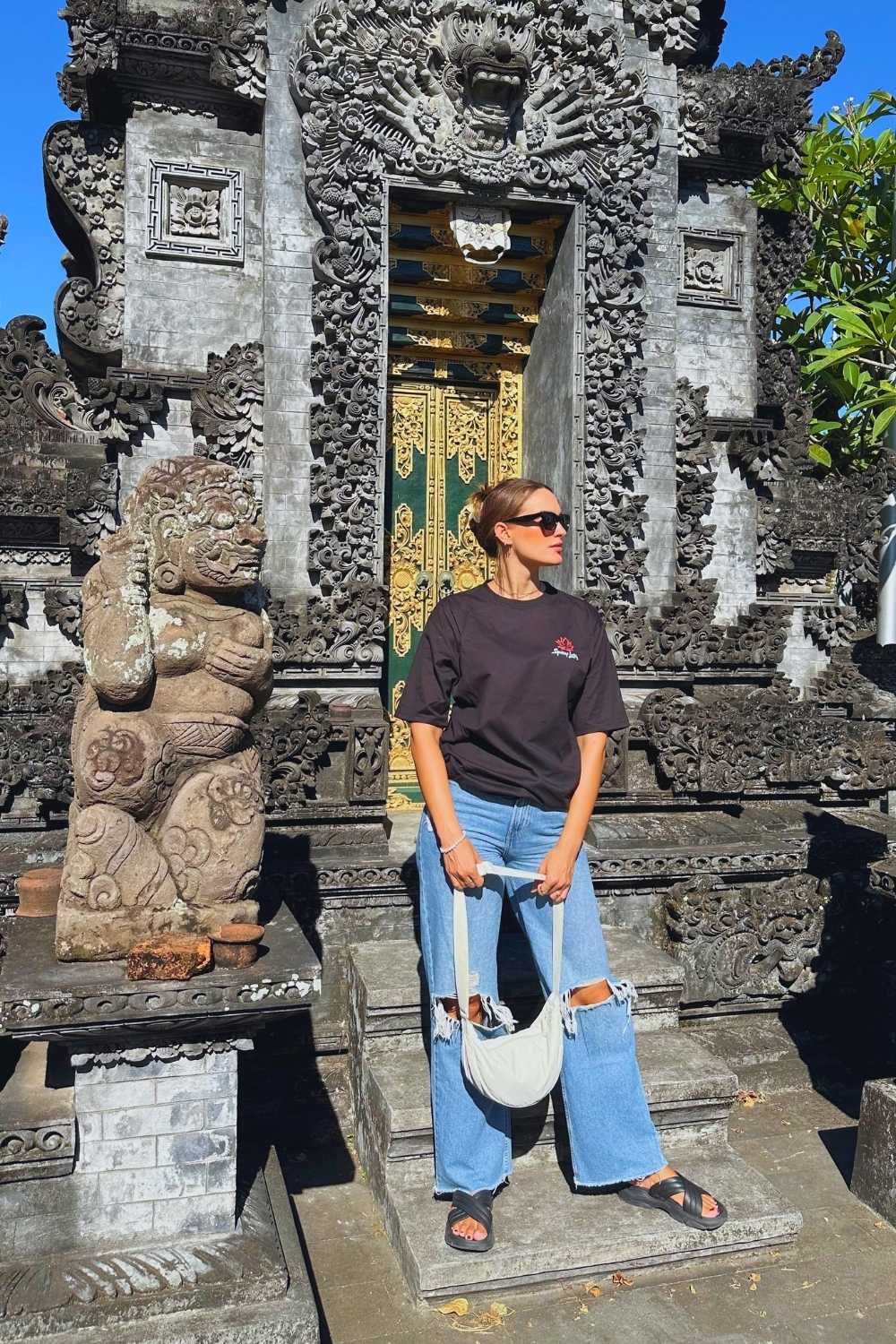 Woman standing in front of a traditional balinese temple entrance with intricate carvings.