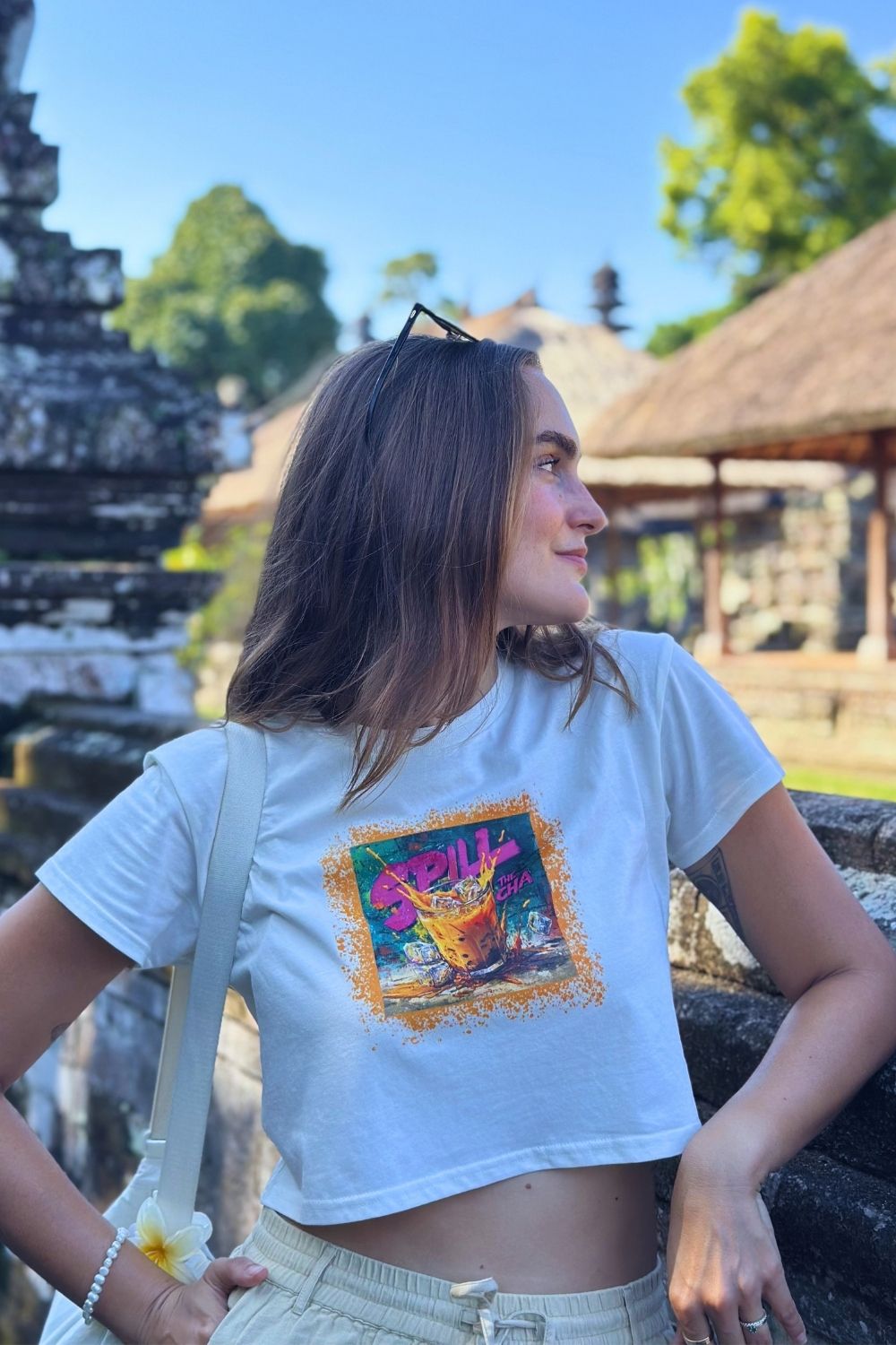 Woman wearing a white crop top shirt with a colorful graphic design in an outdoor setting.
