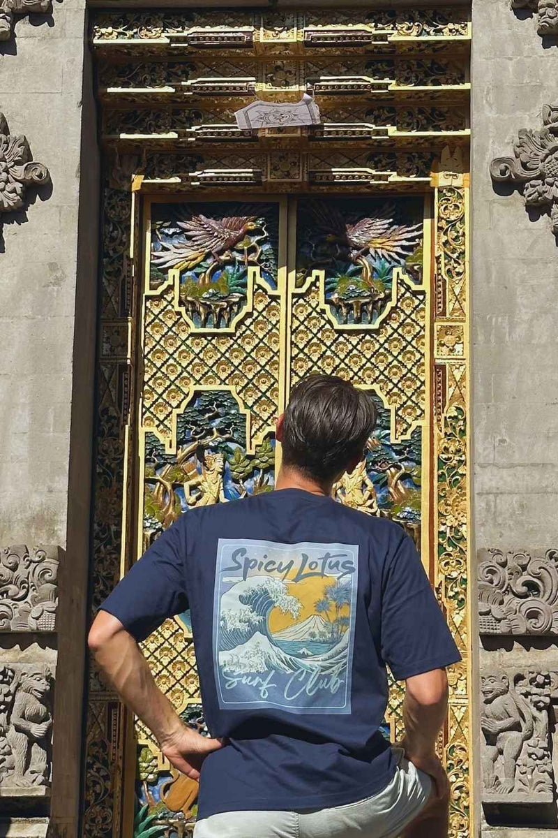 A man viewed from behind wearing a navy blue Spicy Lotus t-shirt with a large graphic print on the back, standing in front of an ornate golden and blue door.