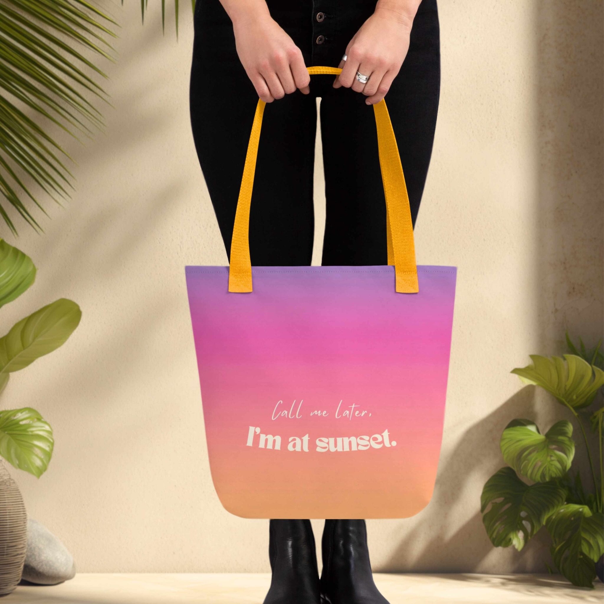 Woman holding a colorful tote bag with gradient design and text, surrounded by plants.