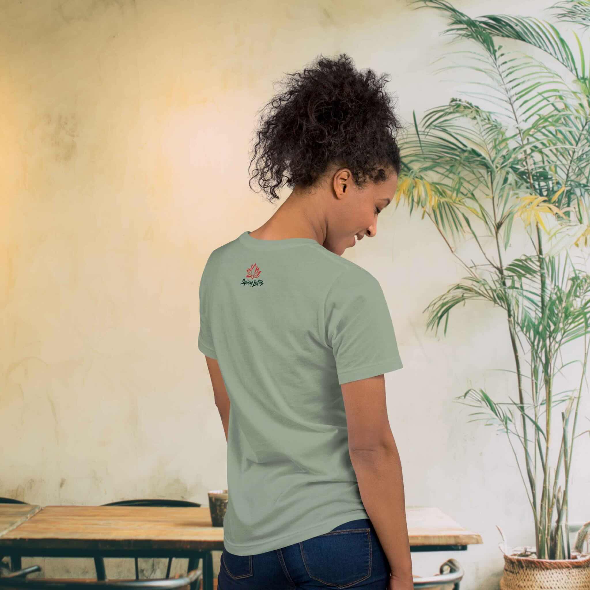 Woman wearing a green t-shirt with a logo, standing in a room with a plant and table.