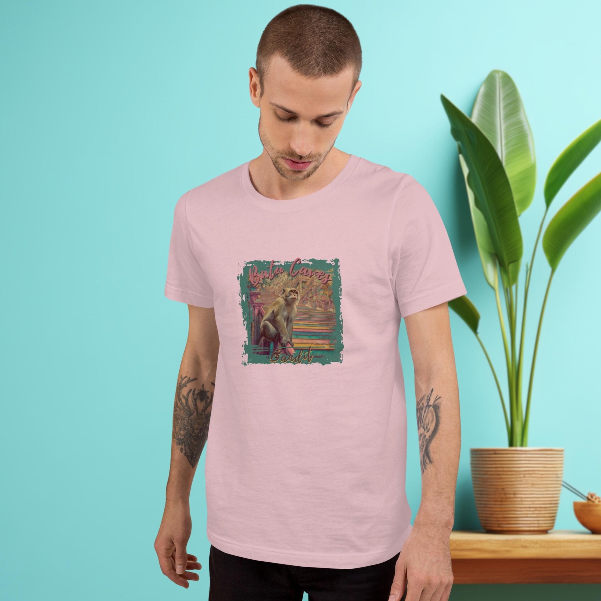 Batu Caves Bandit monkey front print t-shirt on a man in front of turquoise wall