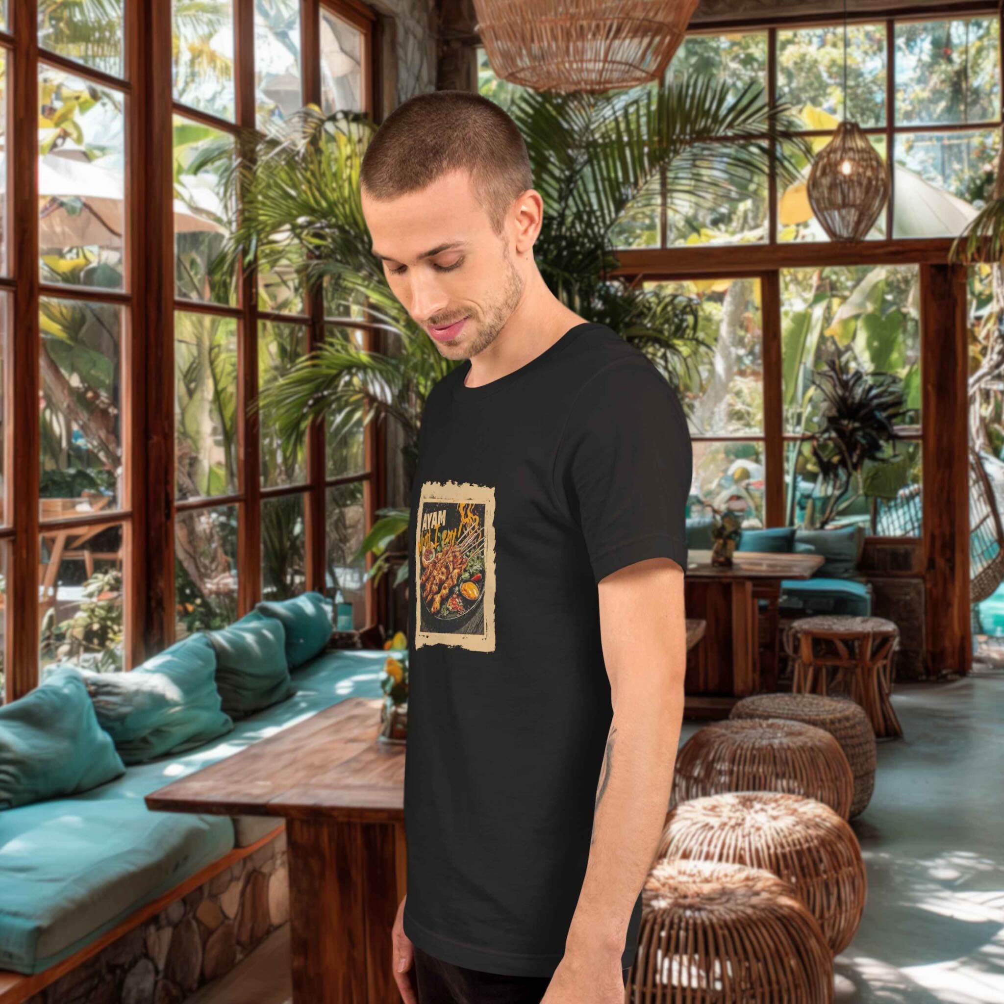 Man wearing a black t-shirt with a graphic design of chicken sate in a tropical-themed indoor setting