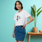 Woman wearing a white t-shirt with text and a coffee graphic, standing against a light blue wall with a plant and small table.