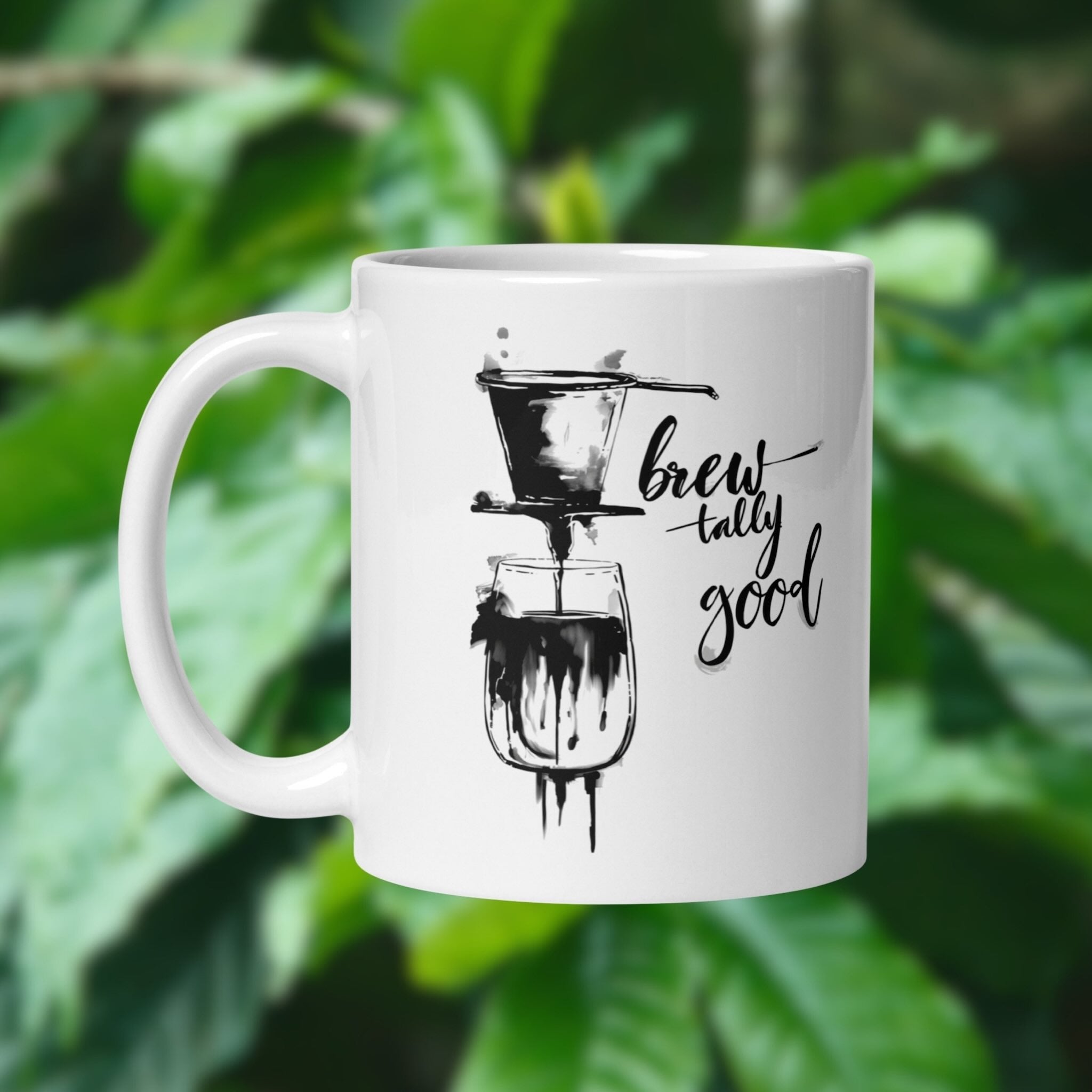 White 11 oz mug with vietnamese phin coffee illustration brewtally Good in the background blurred image of  a coffee plant