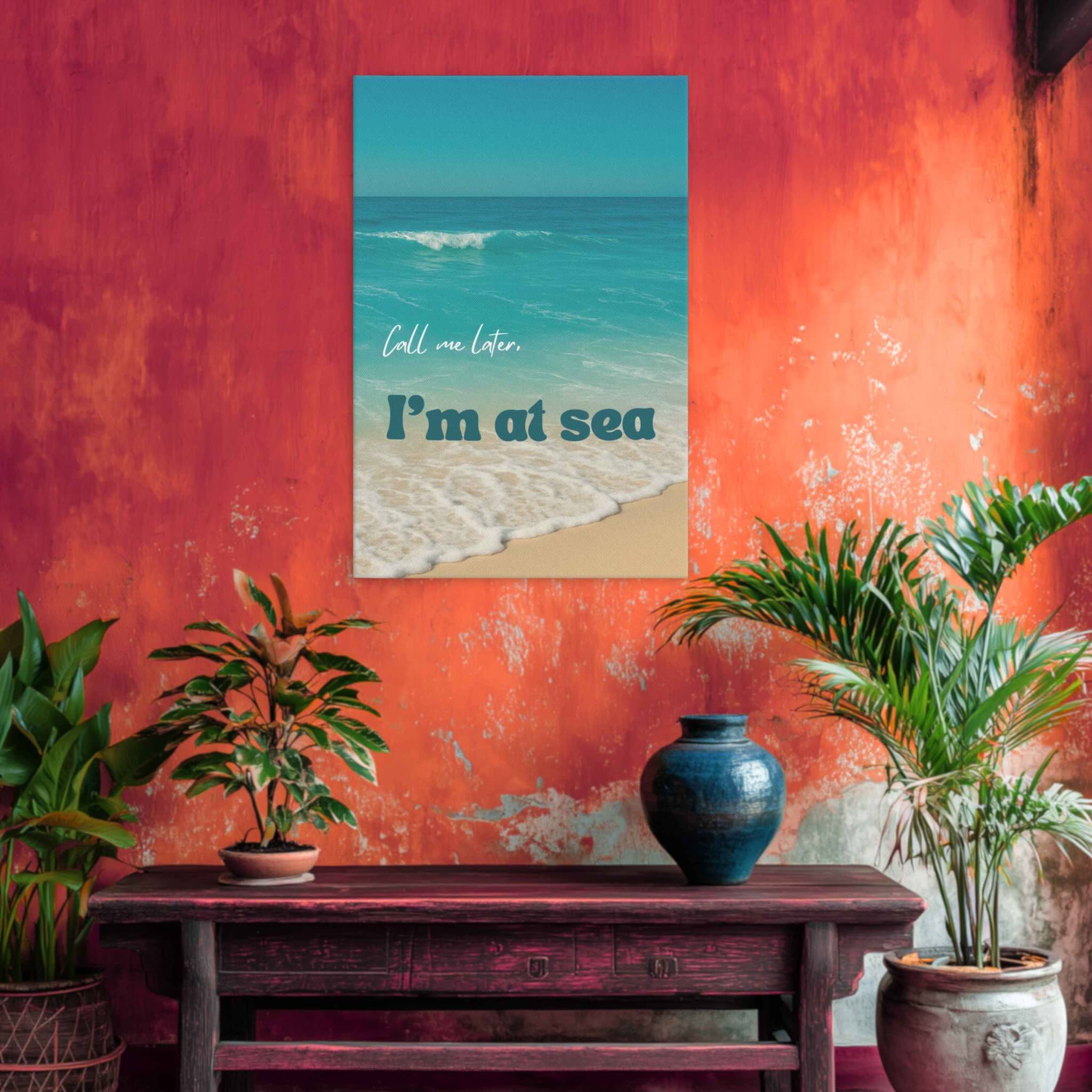 Poster with beach scene and text 'Call me later, I'm at sea' on a red wall with plants and a wooden table.