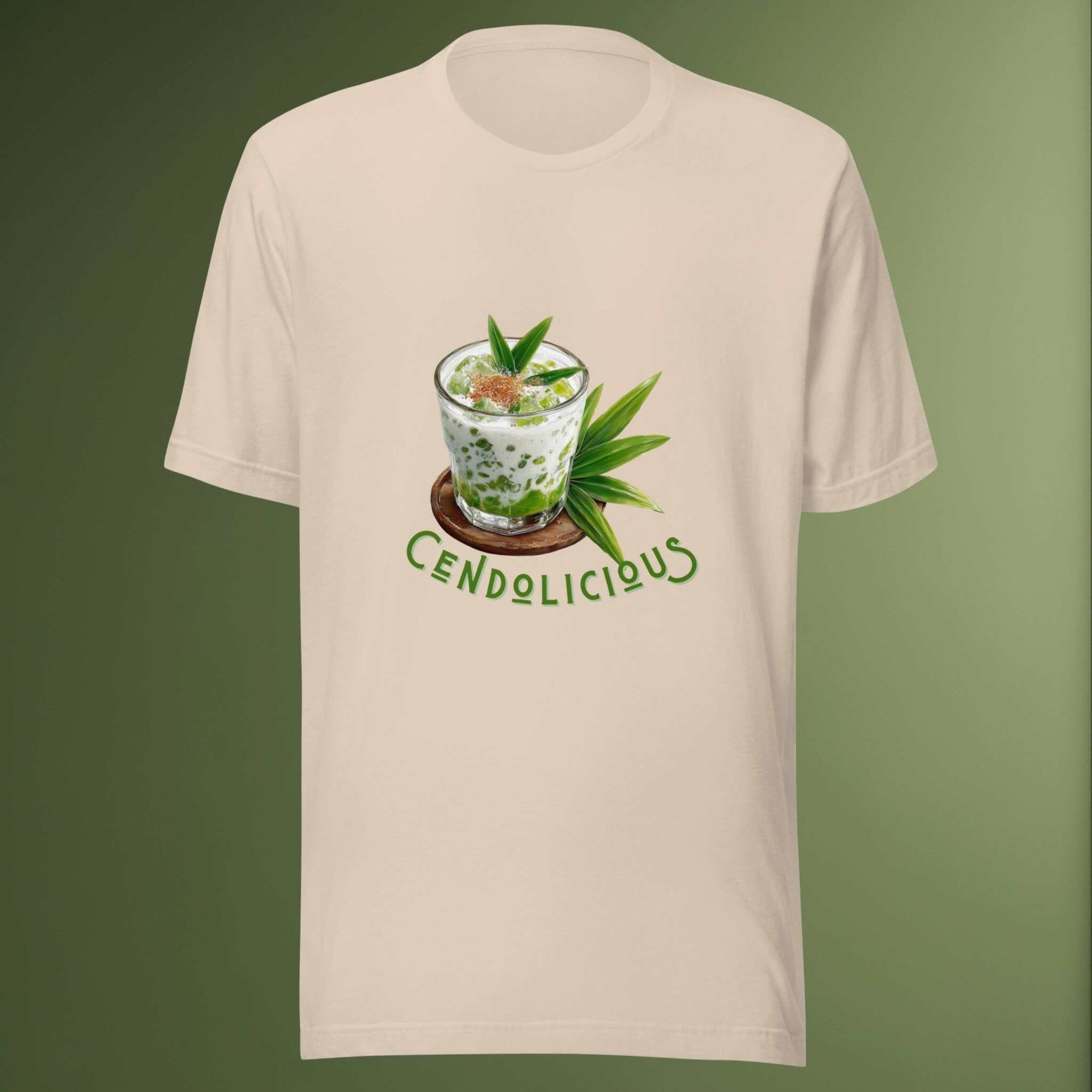 Beige t-shirt with a graphic of a cendol dessert in a glass labeled 'Cendolicious', on a green background.