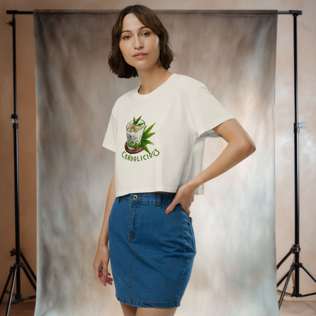 Woman wearing a white t-shirt with a graphic design of indonesian dessert cendol and a blue denim skirt, standing against a neutral backdrop.