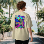 Man wearing a beigeoversized t-shirt with a colorful graphic of two turtles on the back, standing in a tropical setting with palm trees and a beach.