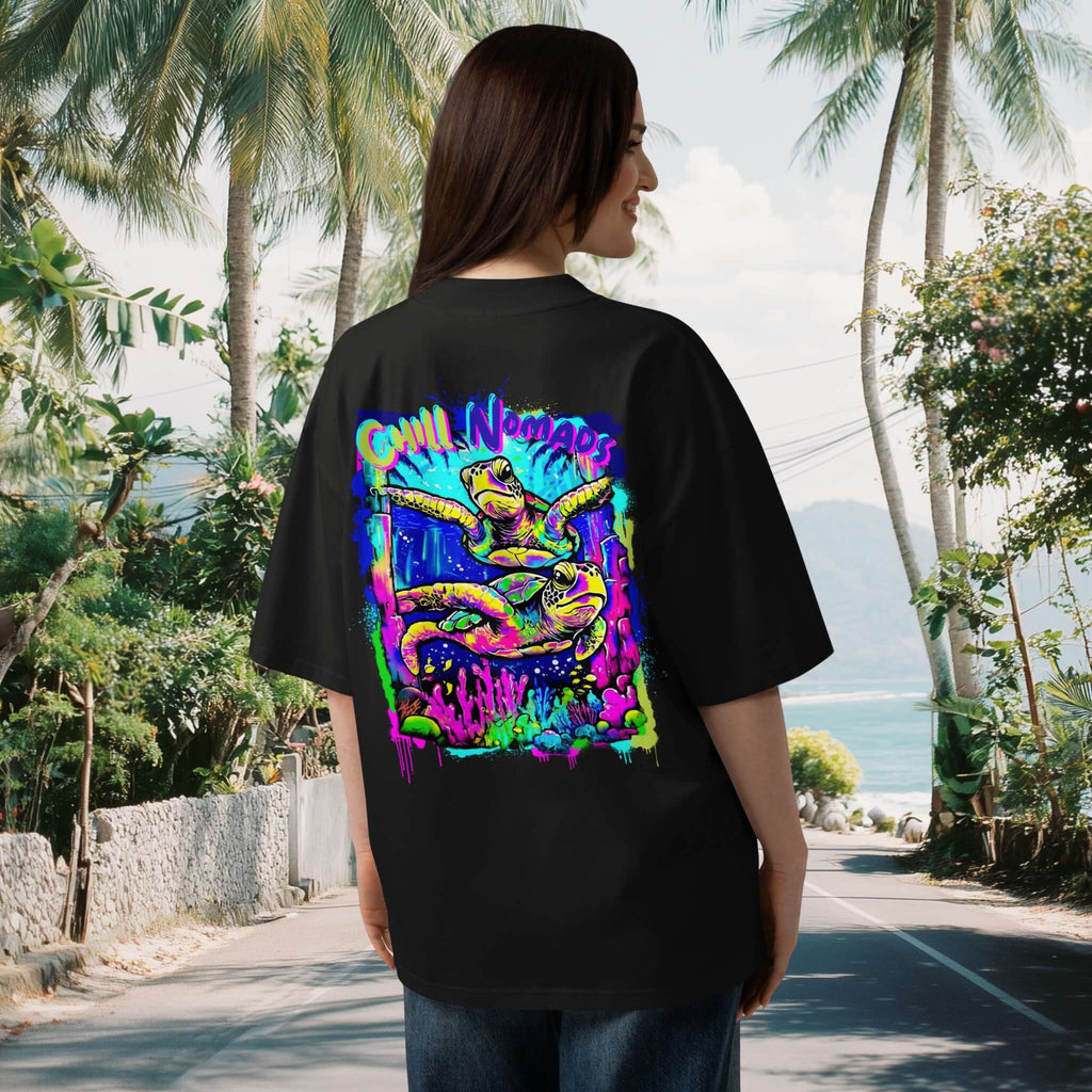 Woman with long brown hair wearing a black tee with dropped shoulders with a colorful graphic of a colorful reef and two turtles in graffiti style in a tropical setting