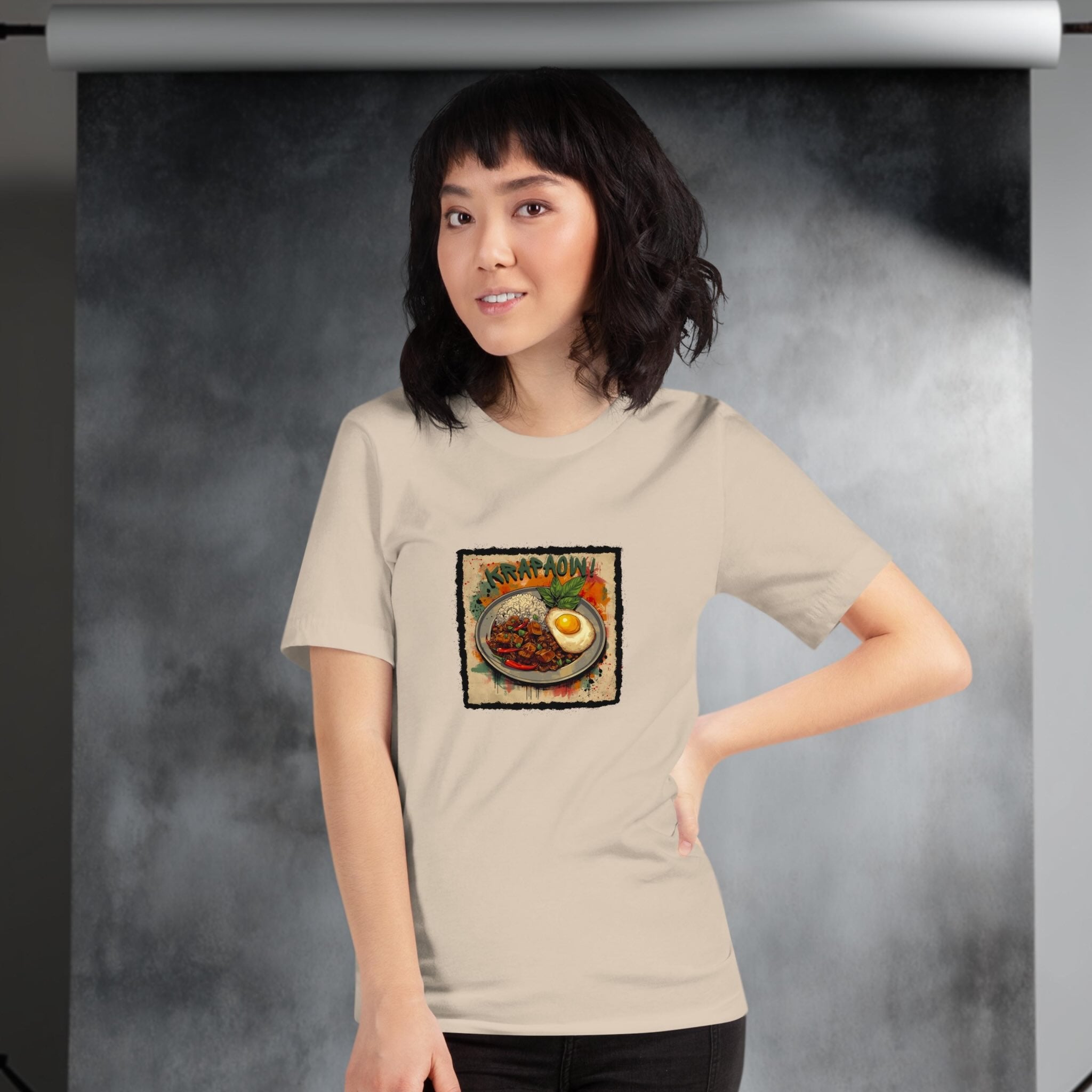 Woman wearing a beige t-shirt with a graphic design of Tahi dish Pad Krapao on a gray background
