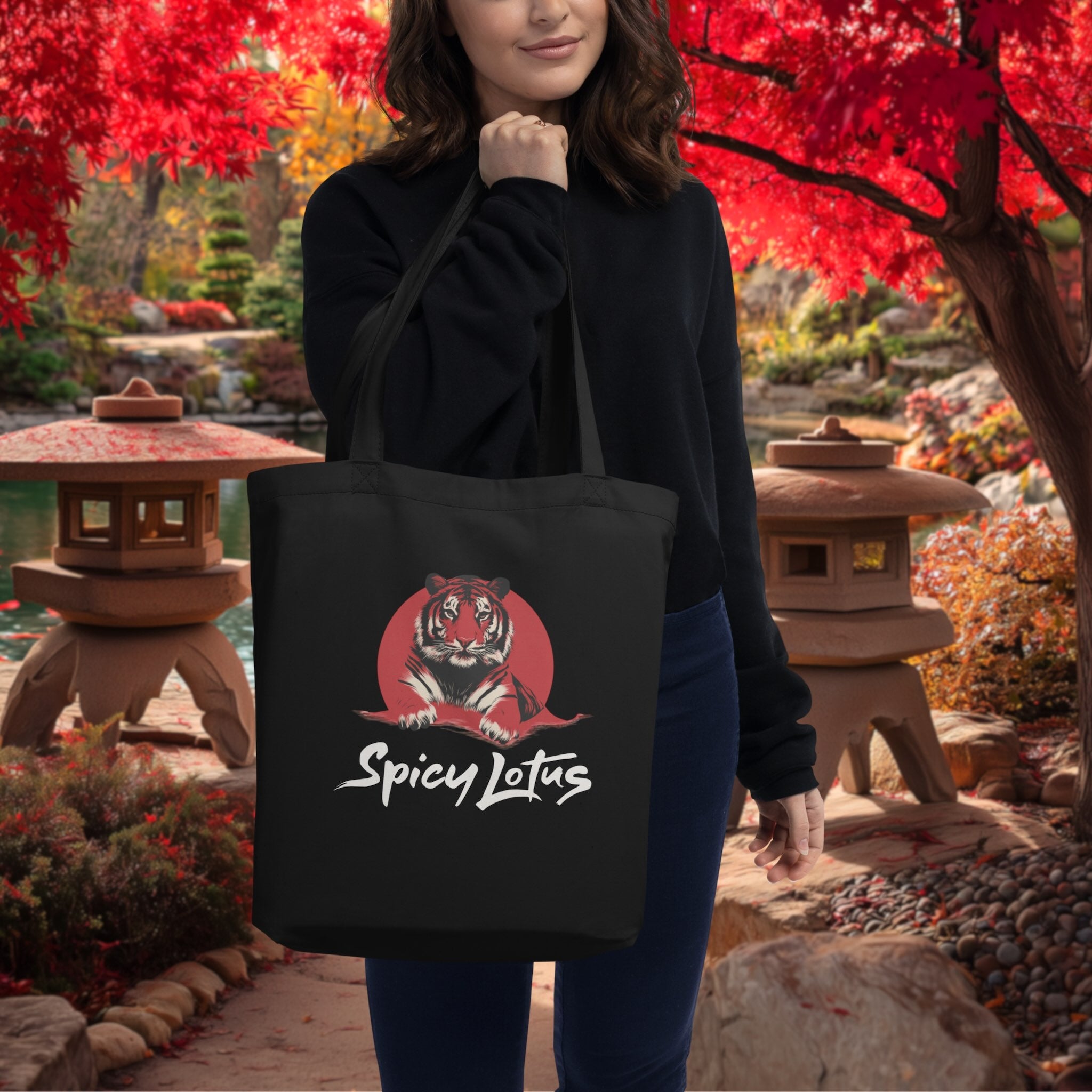 Woman holding a black tote bag with a tiger logo and 'Spicy Lotus' text in an outdoor setting with red foliage.