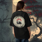 Person wearing an oversized black t-shirt with a graphic design in front of a japanese stylized tree background.