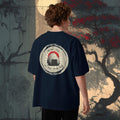 Person wearing an organic oversized navy blue t-shirt with a graphic designo f japanese onigiri and pun, standing in front of a japanese stylized tree background.