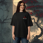 Woman wearing a 100 % organic cotton black t-shirt with a logo in front of a decorative wall.