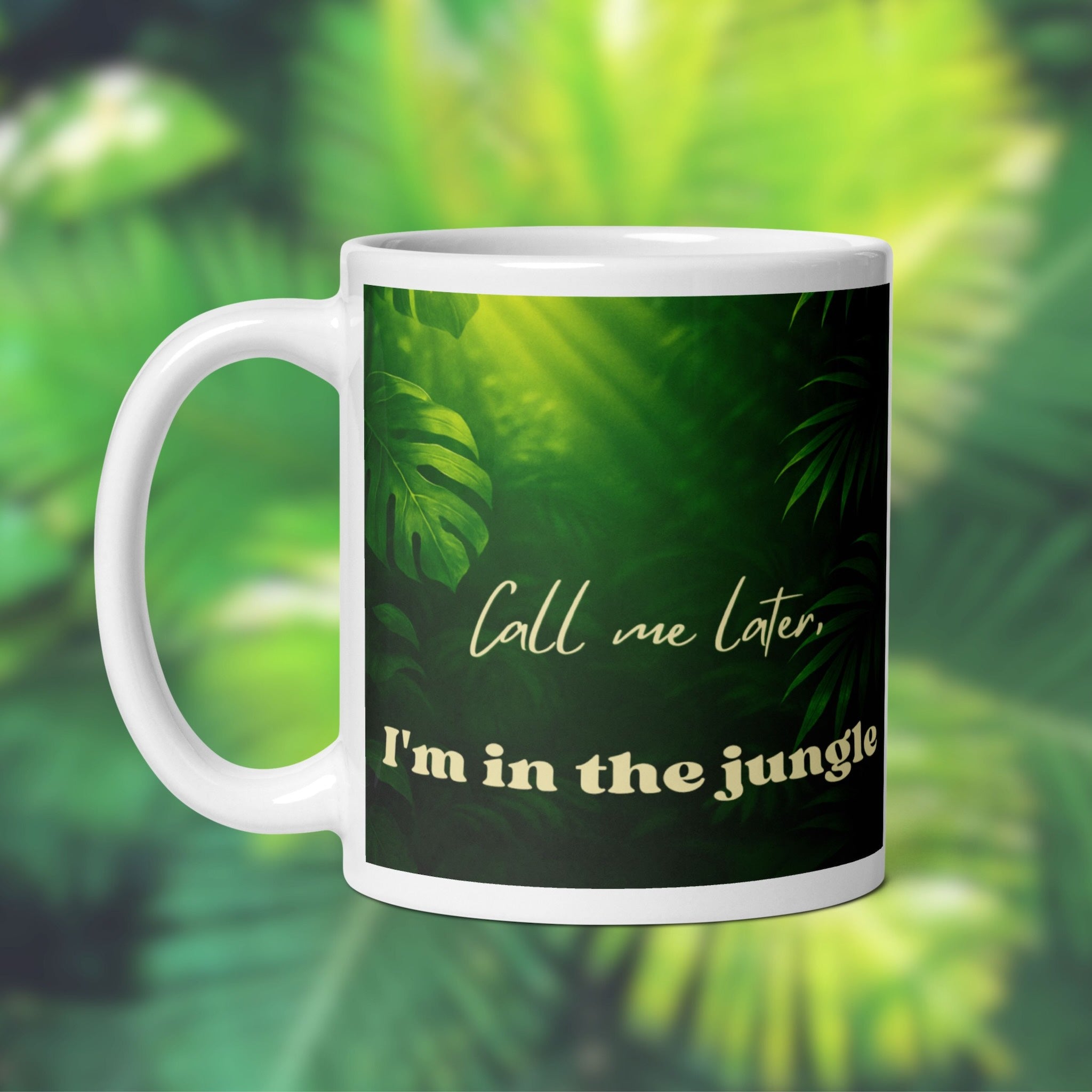 White mug with green leafy pattern and text 'Call me later, I'm in the jungle' on a blurred green foliage background.