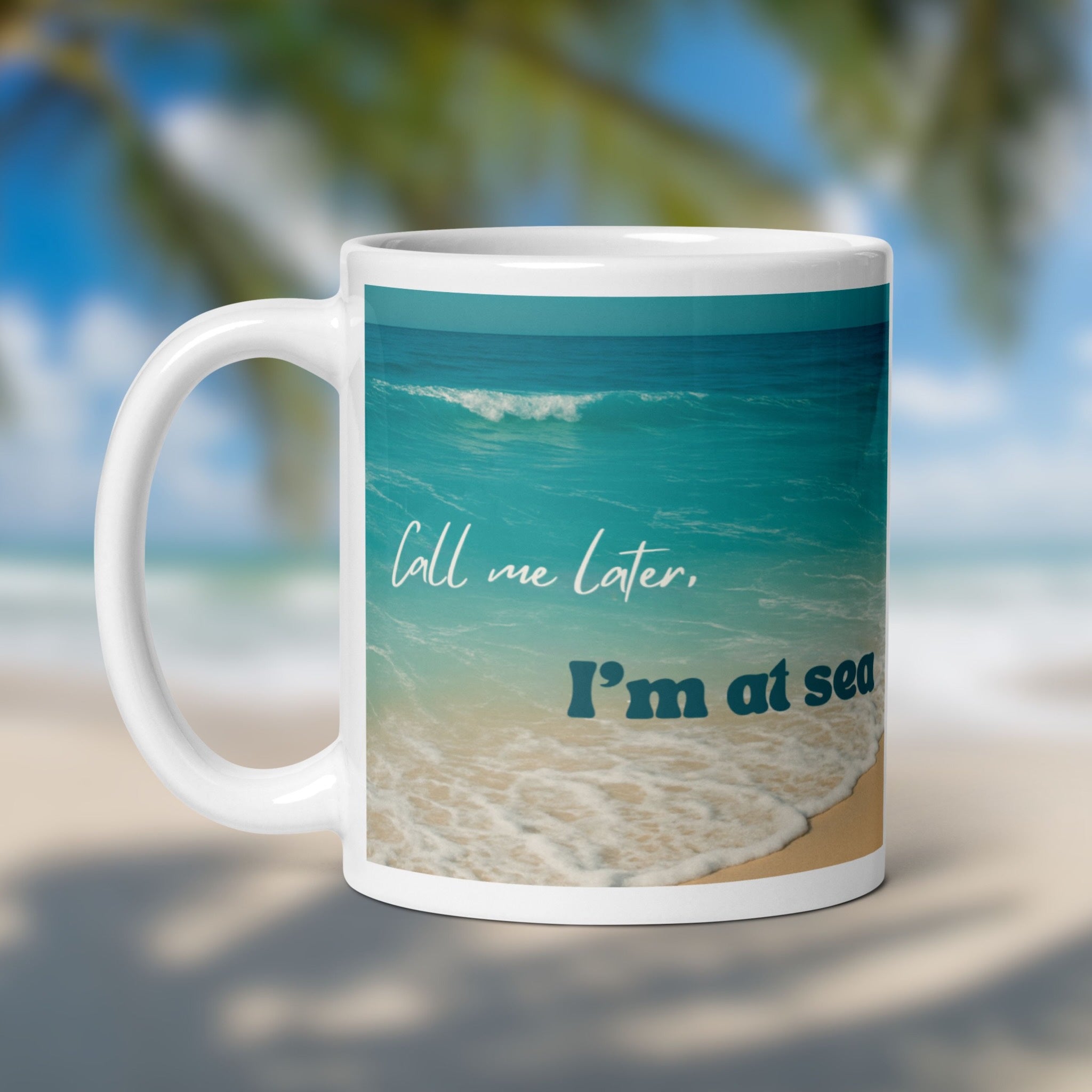 Mug with beach design and text 'Call me later, I'm at sea' on a blurred beach background