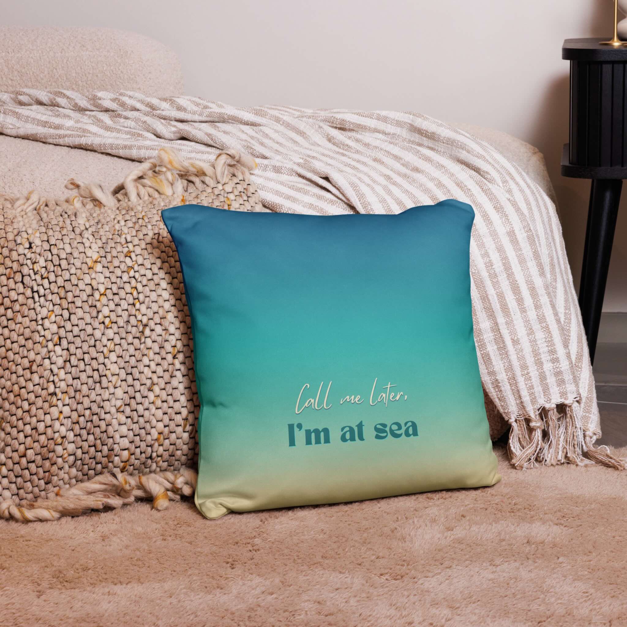 Teal pillow with 'Call me later, I'm at sea' text on a bed with beige bedding.