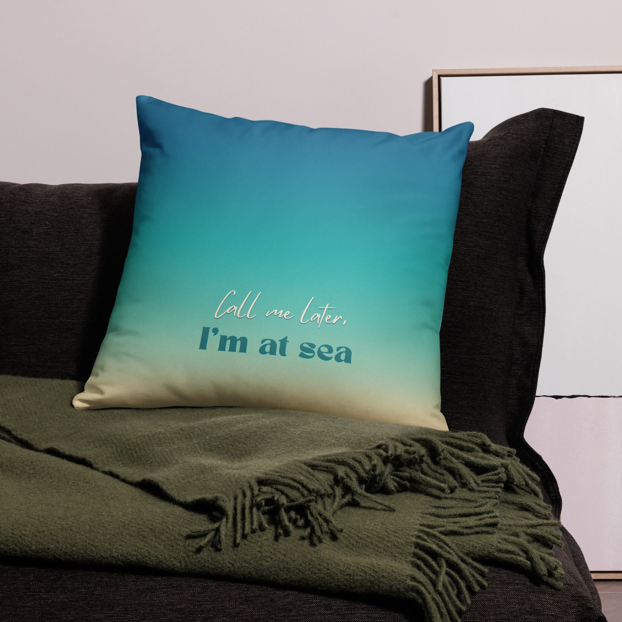 Blue pillow with 'Call me later, I'm at sea' text on a couch with a green blanket.