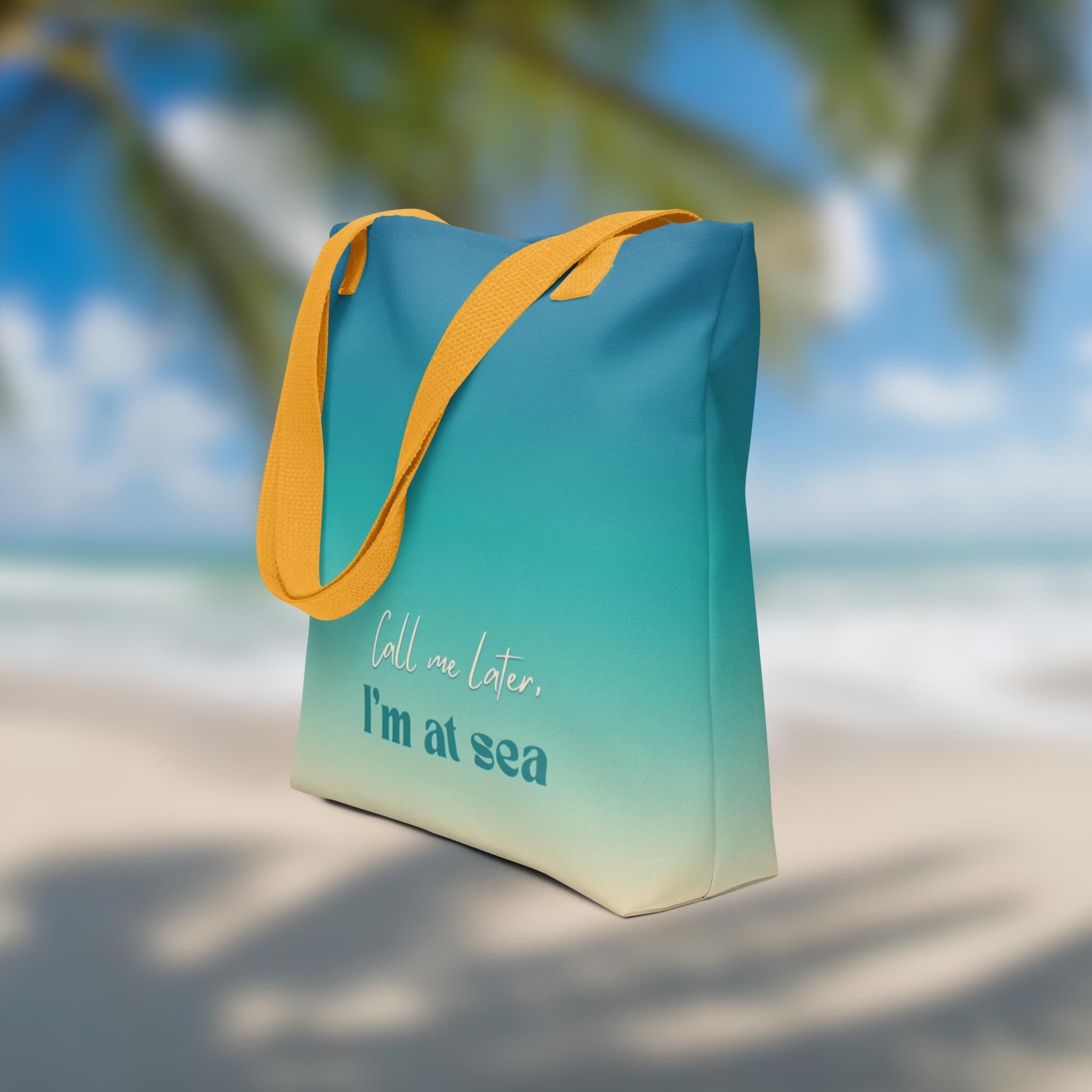 Blue and yellow tote bag with 'Call me later, I'm at sea' text on a beach background