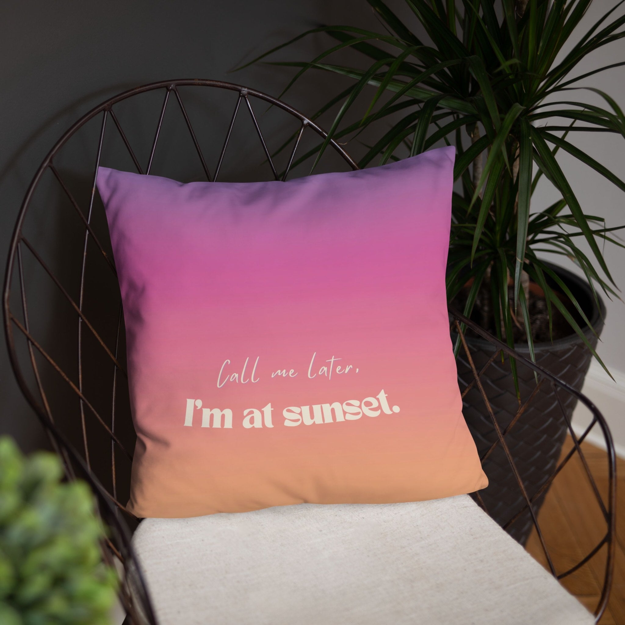 Gradient pillow with 'Call me later, I'm at sunset' text on a chair with a plant in the background
