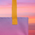 Close-up of a purple bag with a yellow strap against a colorful sunset background