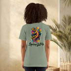 Person wearing a green t-shirt with a colorful lizard design and 'Spicy Lotus' text, standing against a neutral wall with a plant.