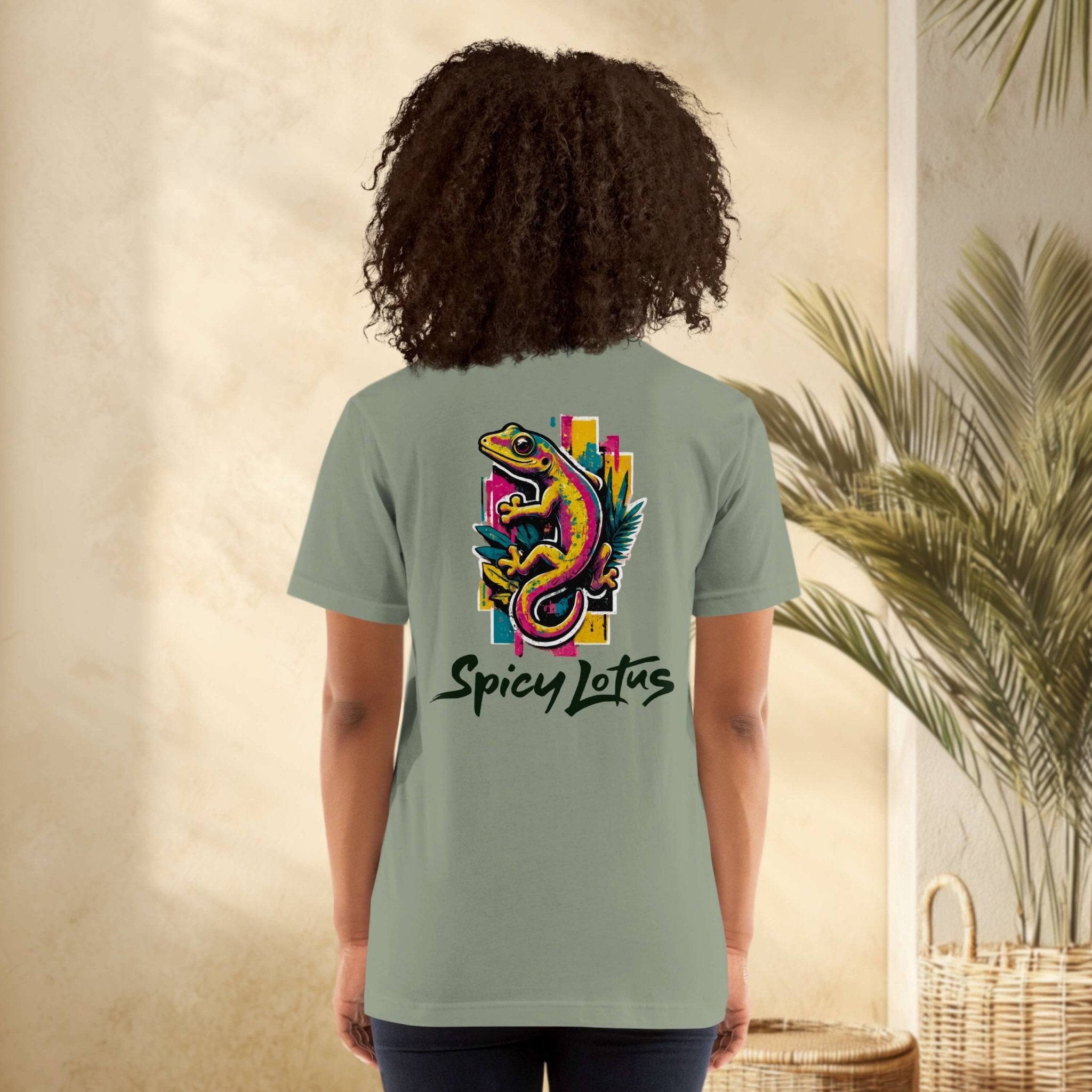 Person wearing a green t-shirt with a colorful lizard design and 'Spicy Lotus' text, standing against a neutral wall with a plant.