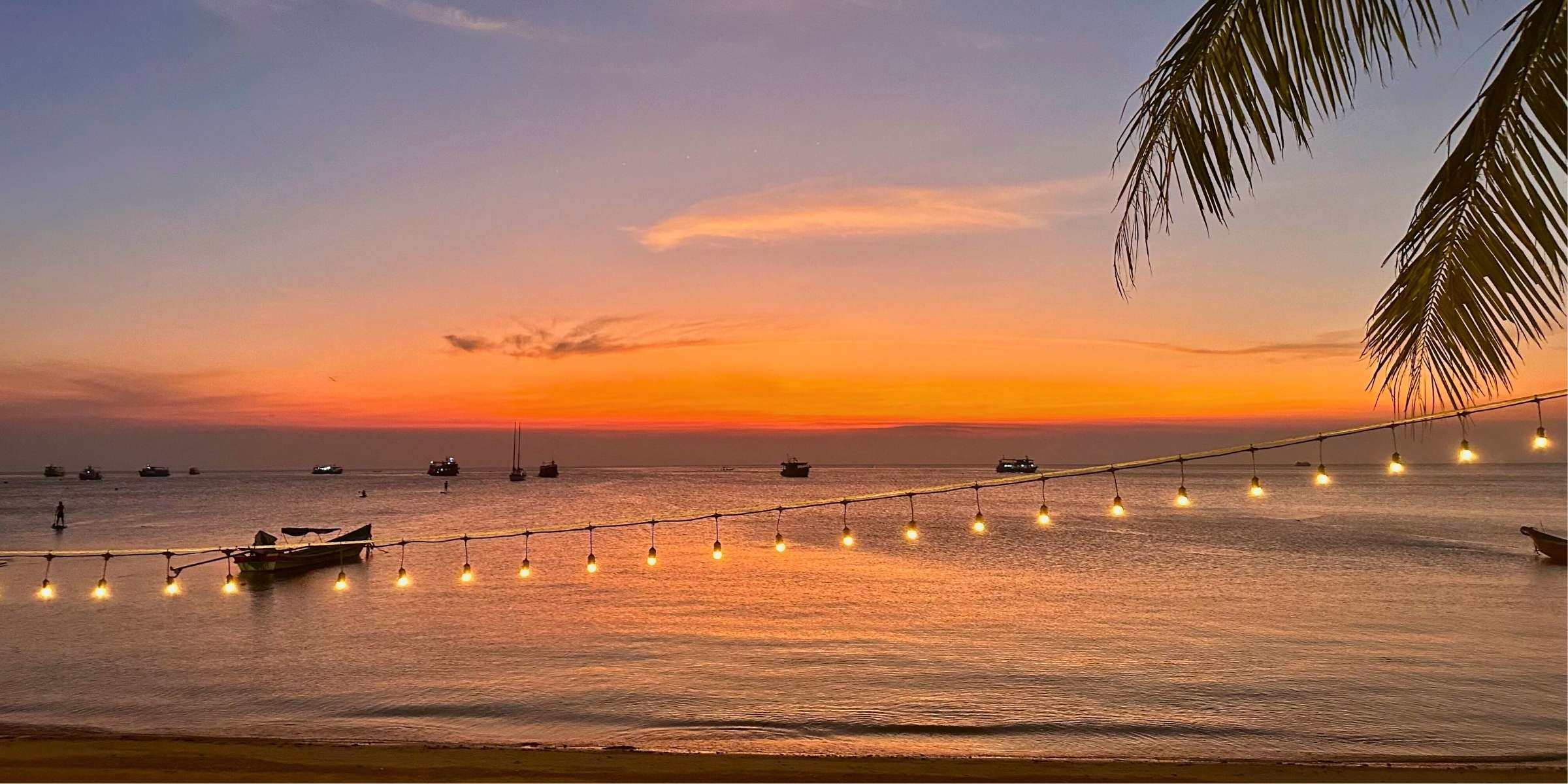 Beach sunset in Koh Tao, Thailand with string lights and palm tree and boats