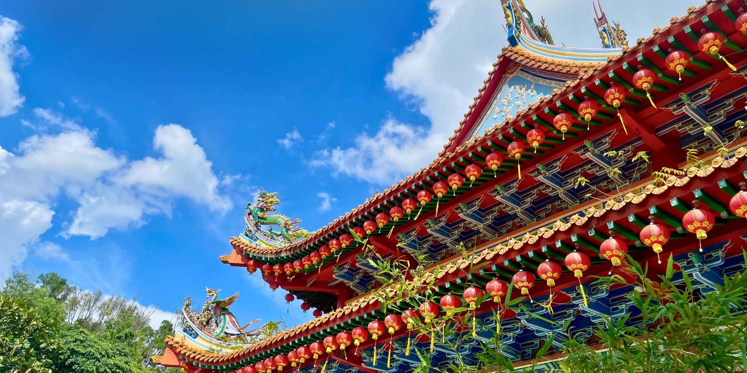 Traditional Chinese temple roof with intricate designs and red lanterns in Kuala Lumpur against a blue sky.