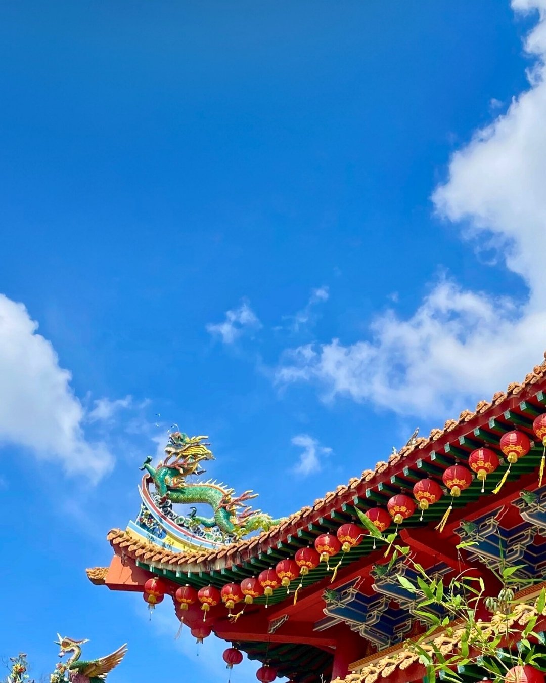 Traditional Chinese temple roof with dragon design and red lanterns in Kuala Lumpur against a blue sky.