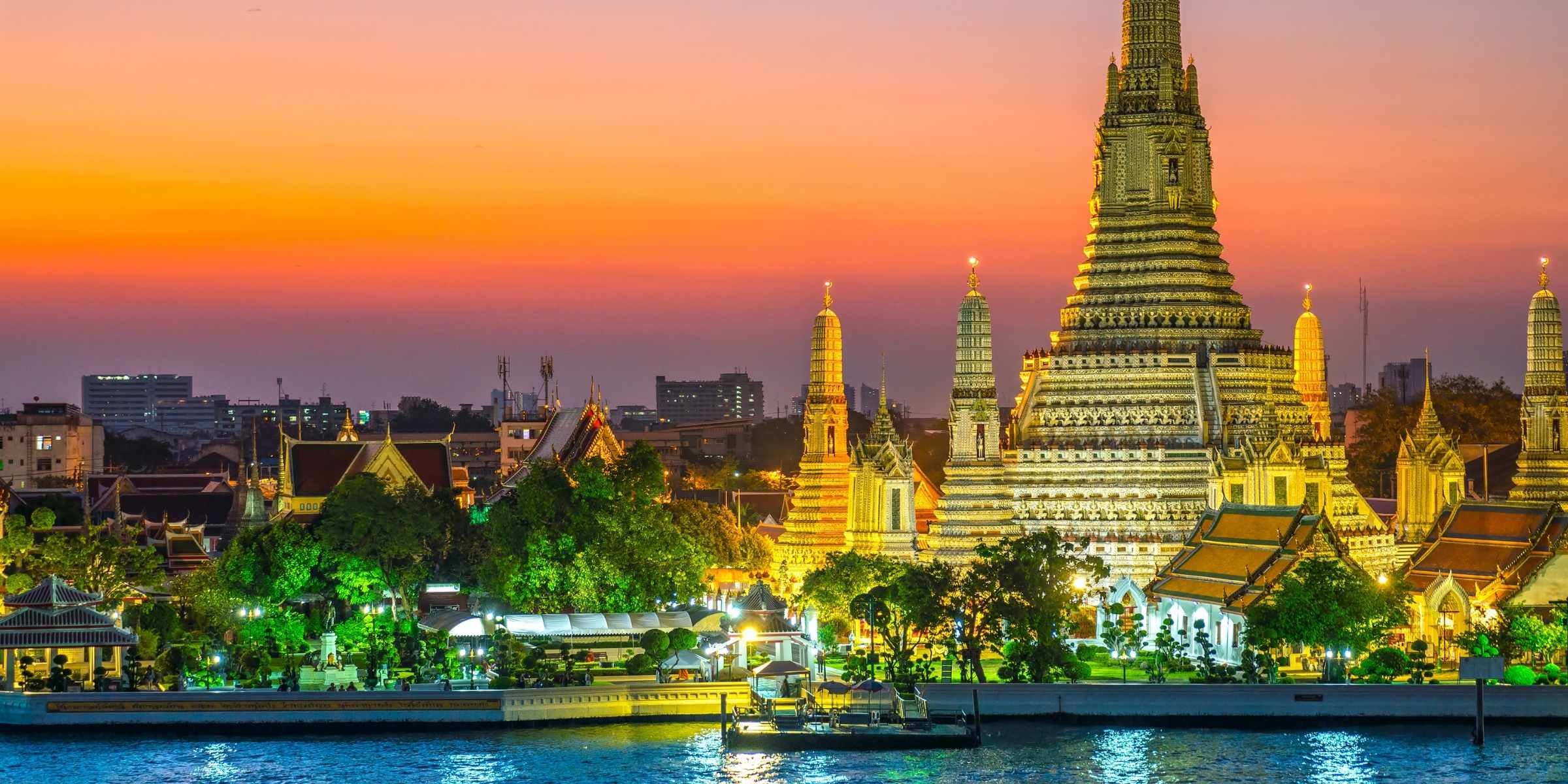 Wat Arun temple at sunset with a pink and, orange and purple sky and water reflection.