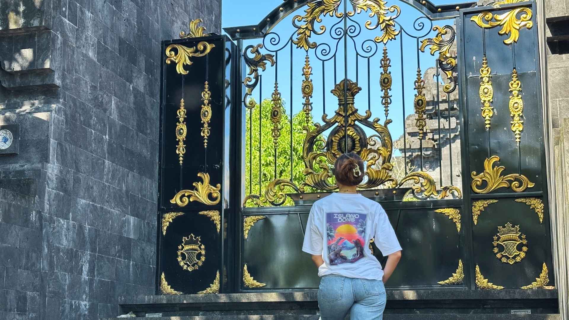 Woman standing in front of an ornate black and gold gate with a back design of a spicy lotus t-shirt