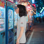 Woman standing in front of a vending machine on a vibrant street at nightm wearing Bella+Canvas ramen pun t-shirt