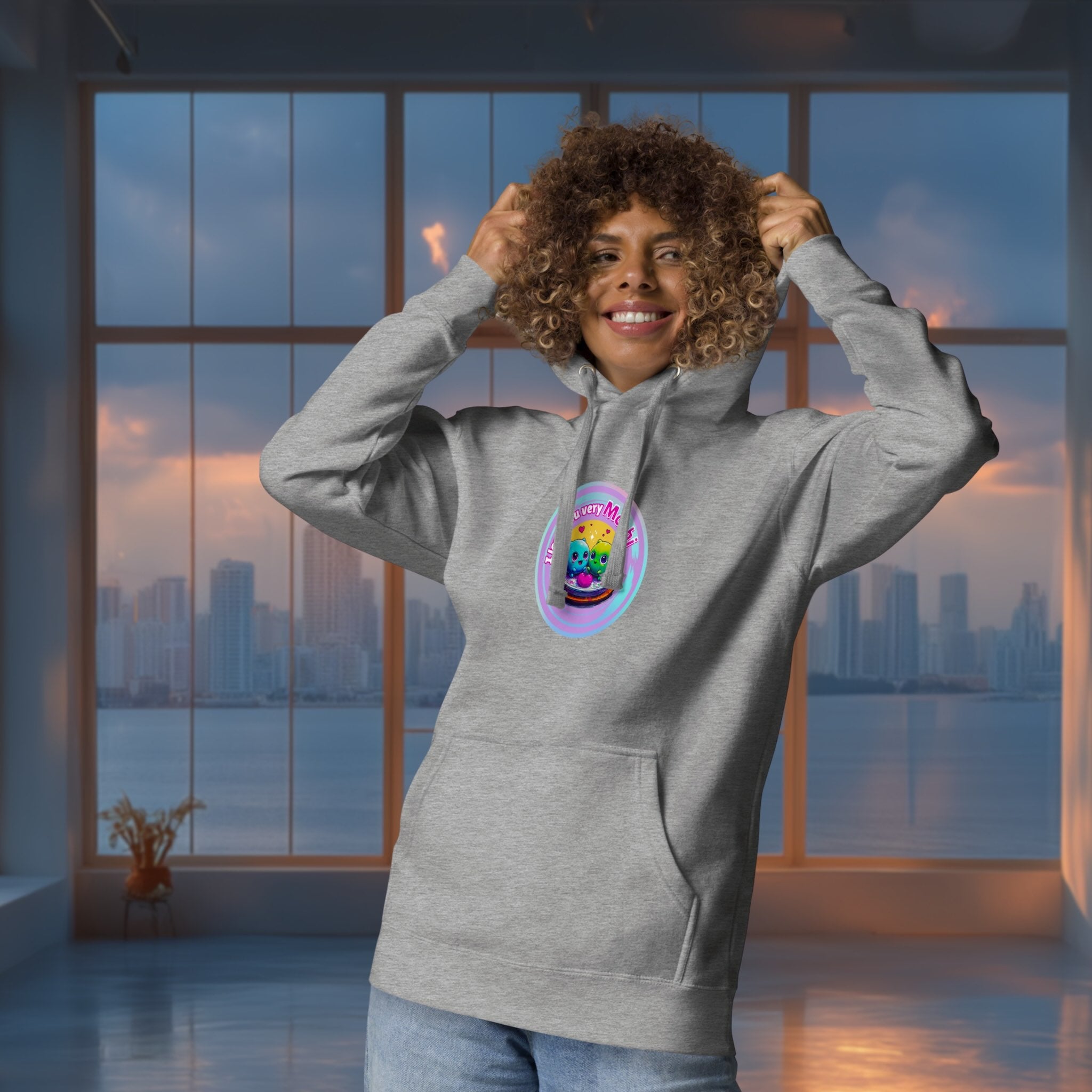 Person wearing a gray hoodie with a colorful graphic  of cute mochis on a cityscape background