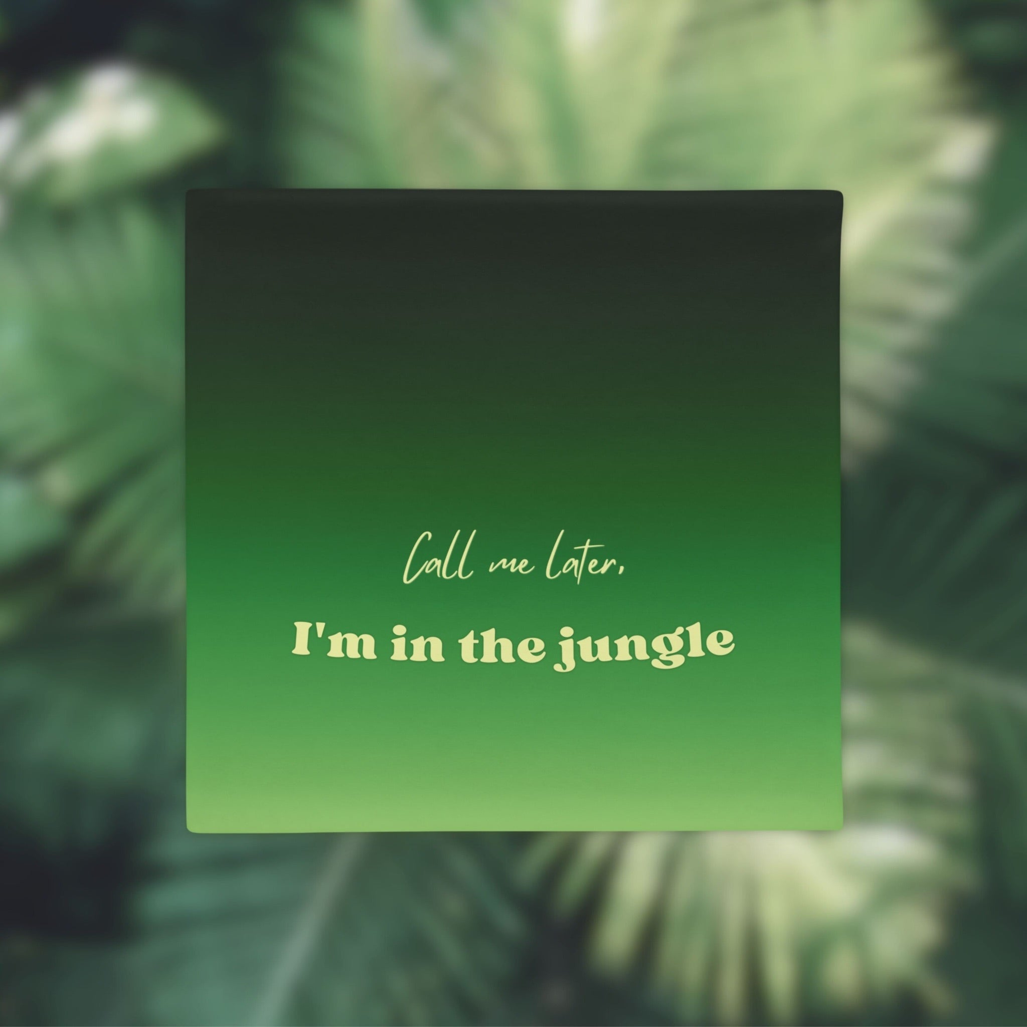 Green square pillow case with text 'Call me later, I'm in the jungle' on a blurred green leafy background