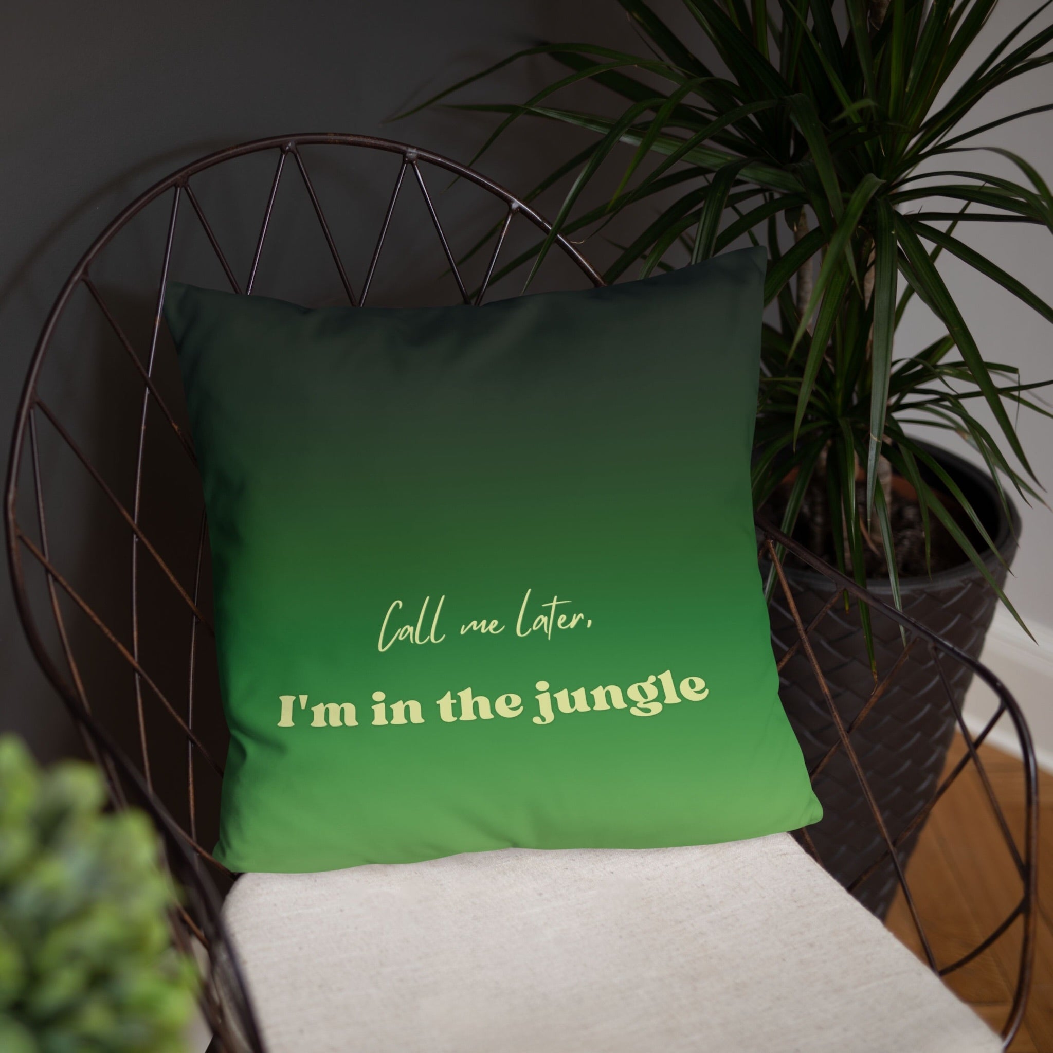 Green pillow with text 'Call me later, I'm in the jungle' on a chair with a plant in the background