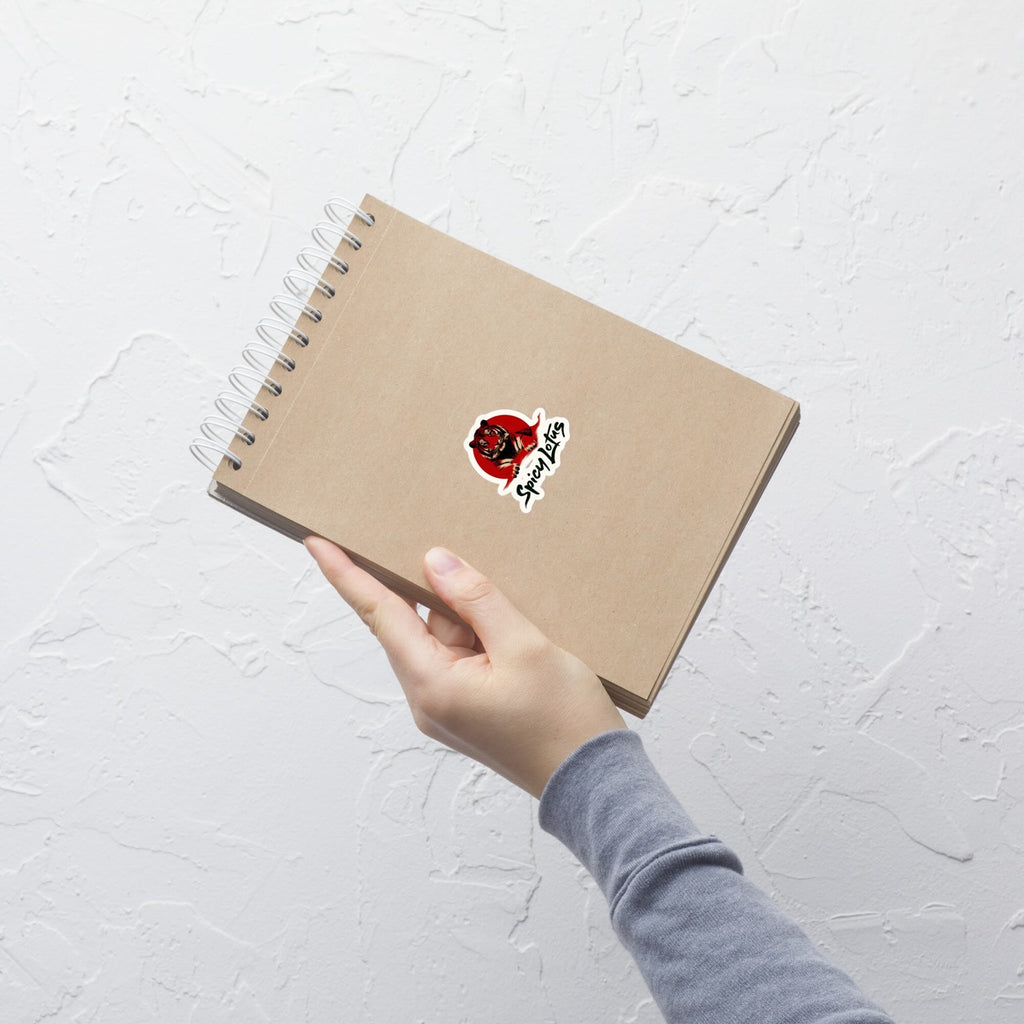 Hand holding a brown notebook with a red and white tiger sticker on a light gray background