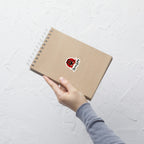 Hand holding a brown notebook with a red and white tiger sticker on a light gray background