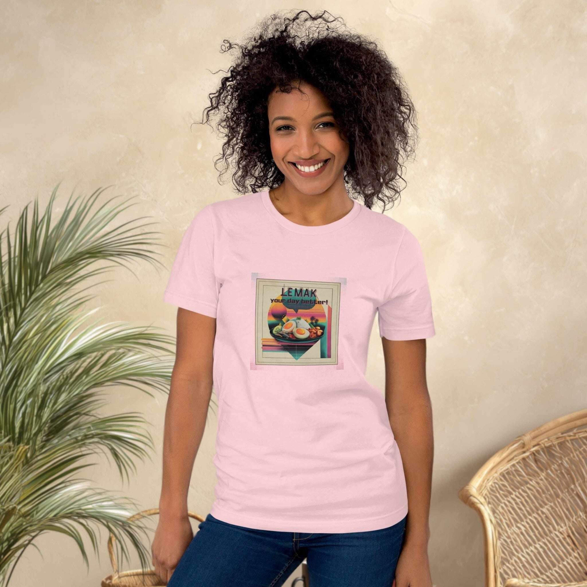 Woman wearing a pink t-shirt with a graphic design, standing against a beige wall with a plant and wicker chair.