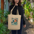 Woman holding a beige tote bag with 'Spicy Lotus Surf Club' design in a garden setting